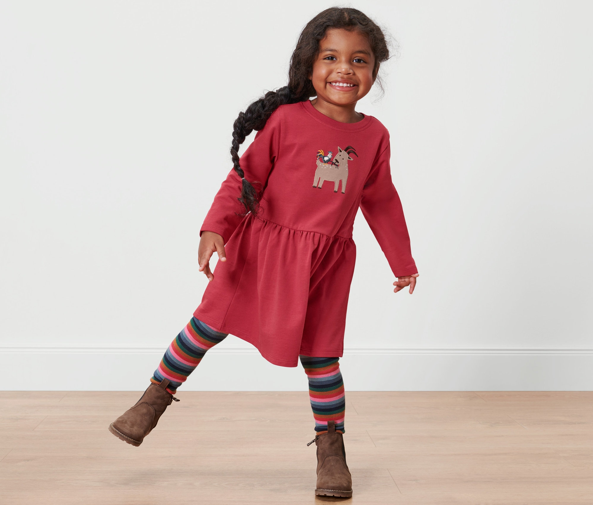 Lächelndes kleines Mädchen posiert in einem roten Kleinkind-Sweatkleid.