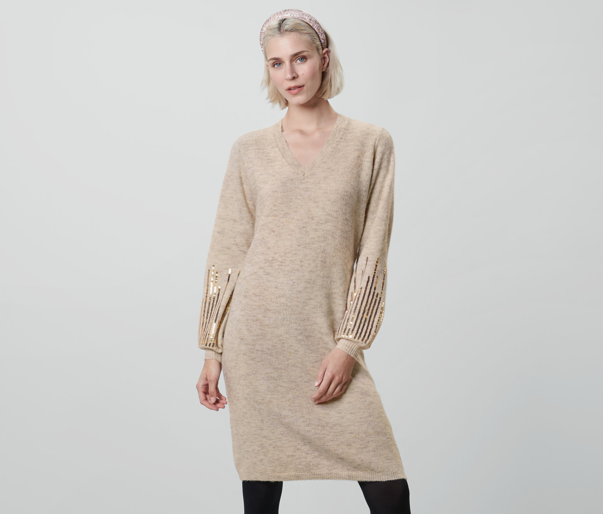 Frau posiert in beigem Strickkleid mit Pailletten.