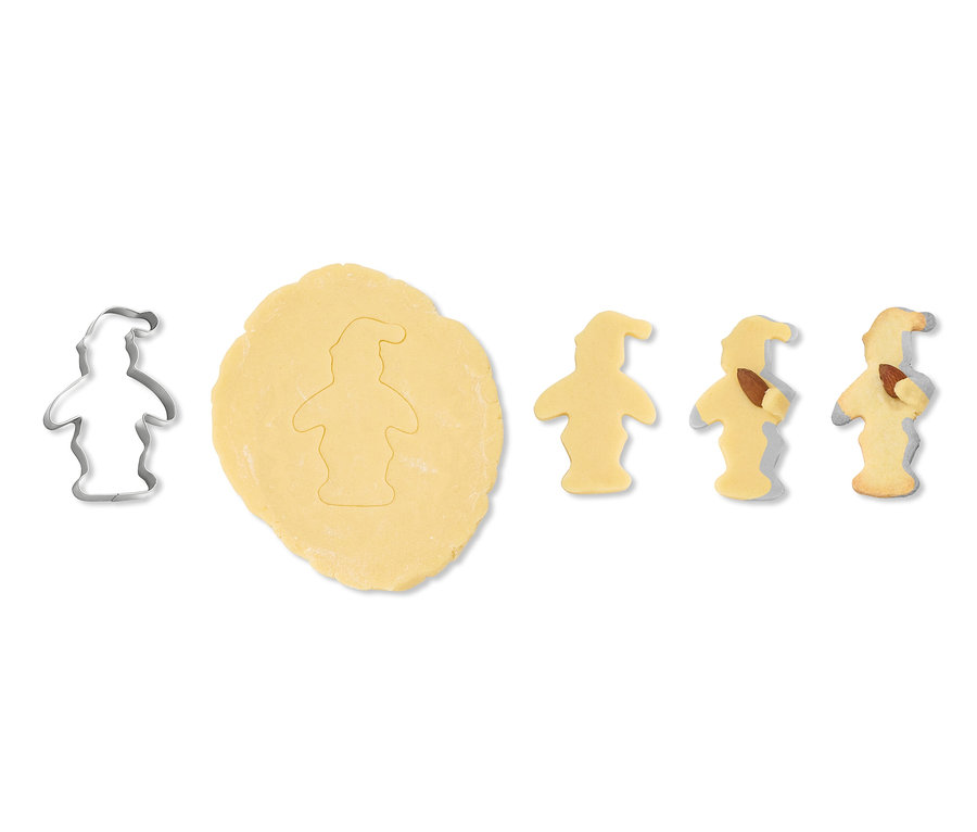 5 Kuschelkeks-Ausstecher: Roher Teig mit einer ausgeschnittenen Figur daneben, eine Metallform und drei gebackene Kekse auf weißem Hintergrund.