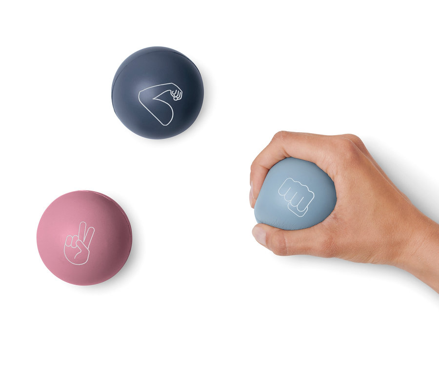 Eine Hand hält einen blauen Antistressball mit einem Faustsymbol. Auf einem weißen Hintergrund liegen ein rosa Ball mit einem Friedenssymbol und ein dunkelblauer Ball mit einem Bizepssymbol. 3 Anti-Stressbälle.