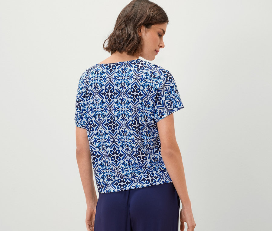 Frau trägt ein blaues bedrucktes Blusenshirt und eine weite Hose.