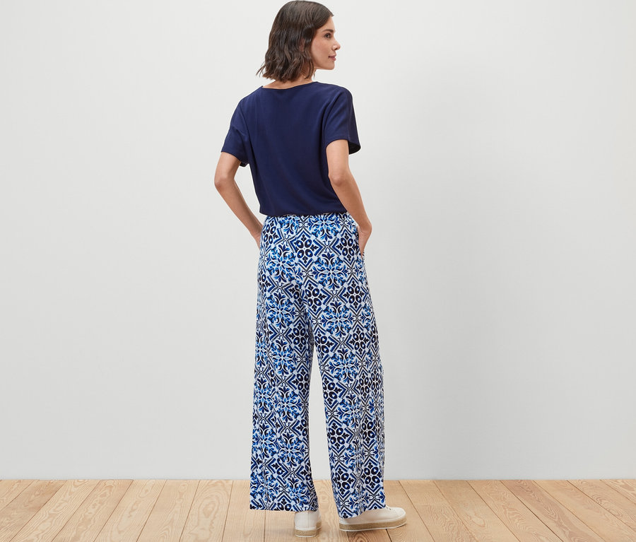 Frau steht mit dem Rücken zur Kamera und trägt eine blaue bedruckte Palazzohose.