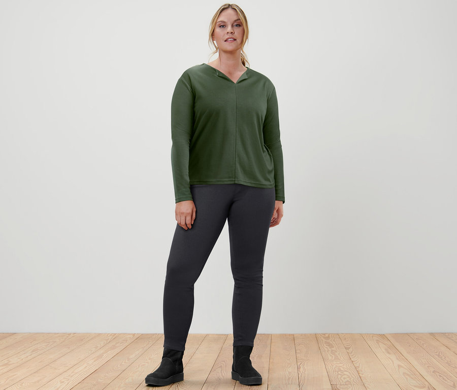 Frau posiert in dunkelgrünem Blusenshirt und Jeggings.