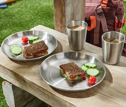Zwei Camping-Teller mit belegten Broten, Gurke und Tomate auf einem Holztisch.