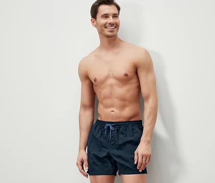 Mann lächelt und trägt Badeshorts.