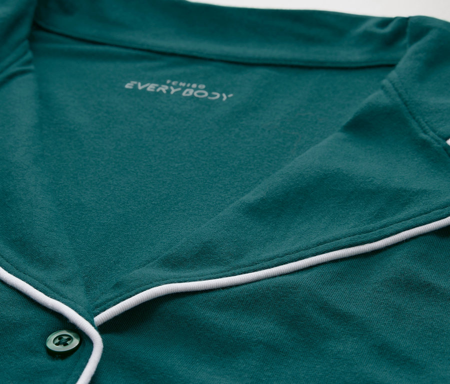 Detailaufnahme eines grünen Pyjamaoberteils mit weißer Paspelierung und Knöpfen.