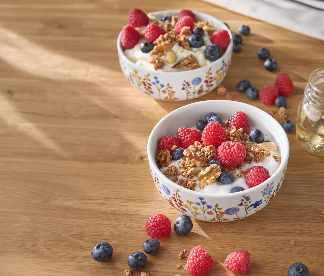 Zwei Schalen Joghurt mit Himbeeren, Blaubeeren und Nüssen auf einem Holztisch.