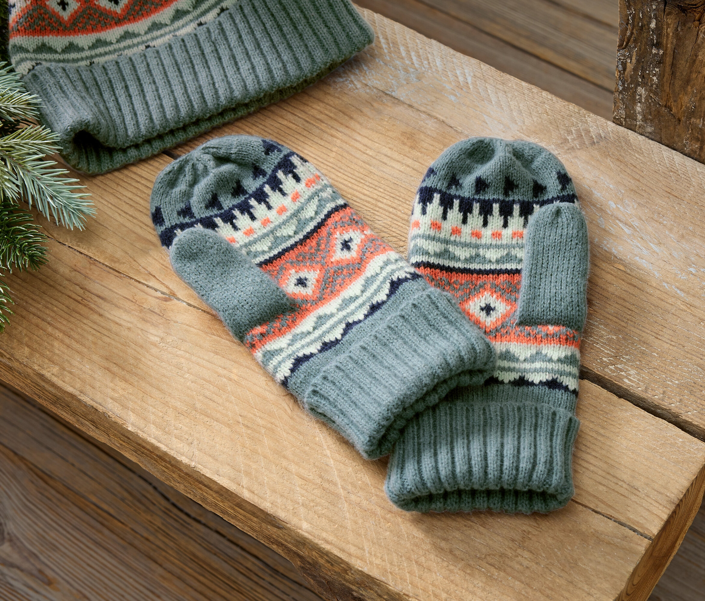 Graue Strickfäustlinge und Mütze mit norwegischem Muster liegen auf einer Holzoberfläche.