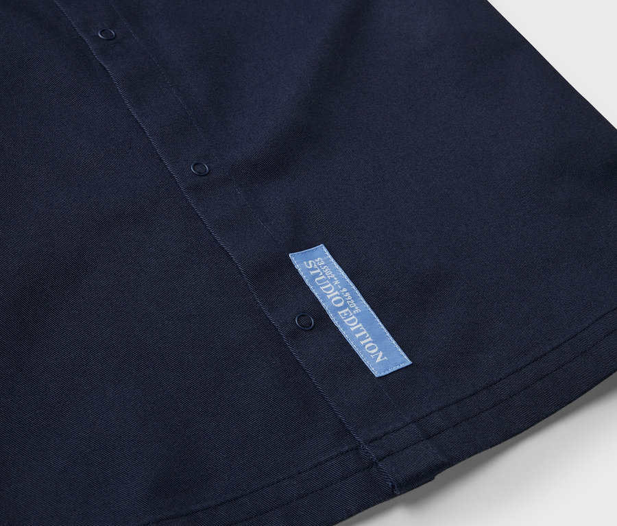 Detailansicht eines dunkelblauen Kinder-Overshirts mit Knöpfen und Studio Edition Etikett.