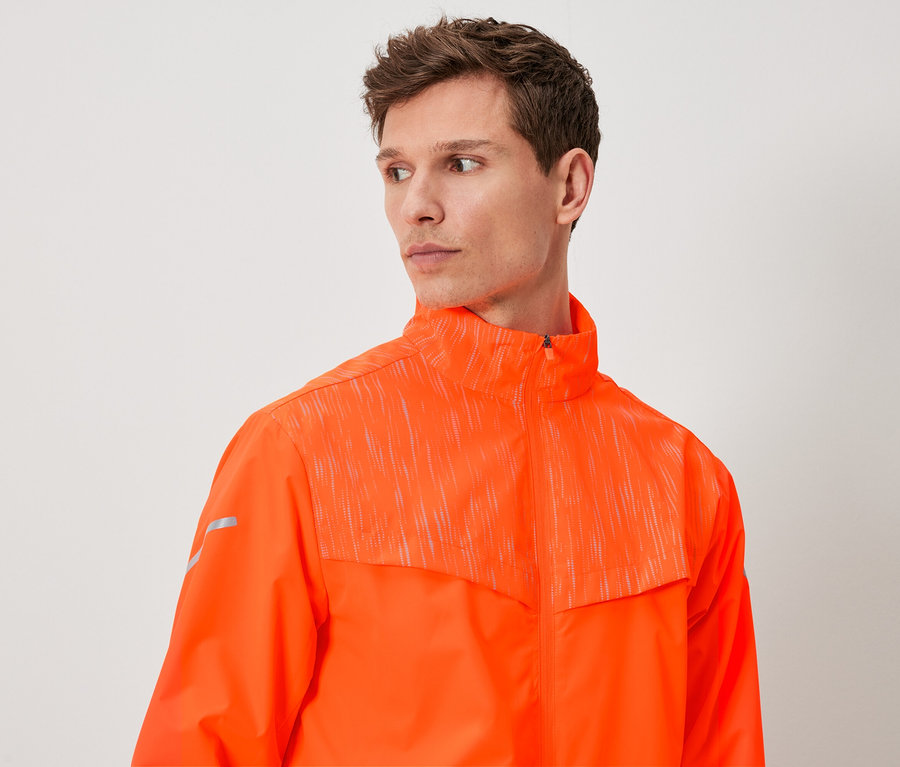 Ein Mann mit braunen Haaren trägt eine orangefarbene Jacke.