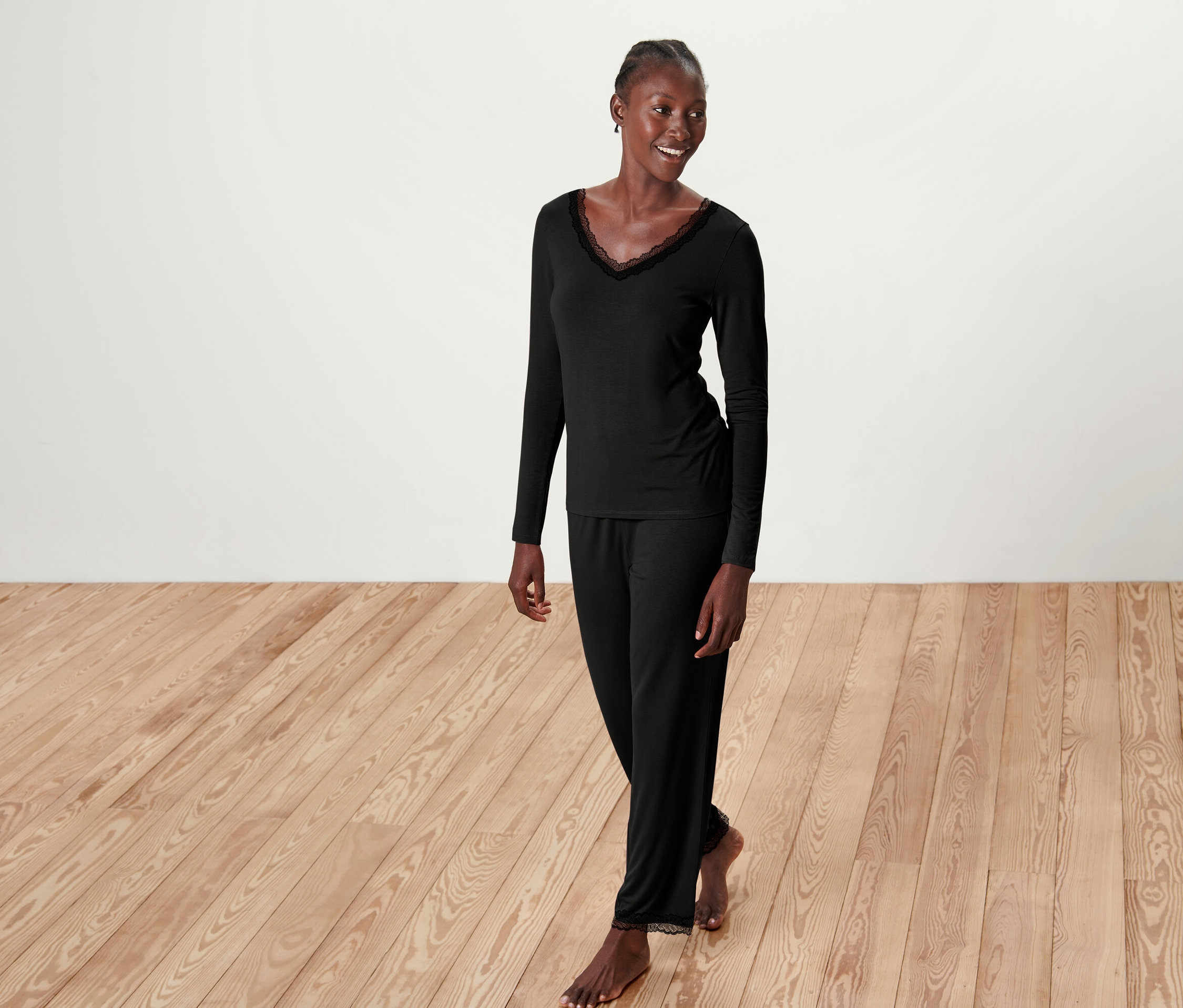 Frau im schwarzen Pyjama mit Spitze posiert auf Holzboden.