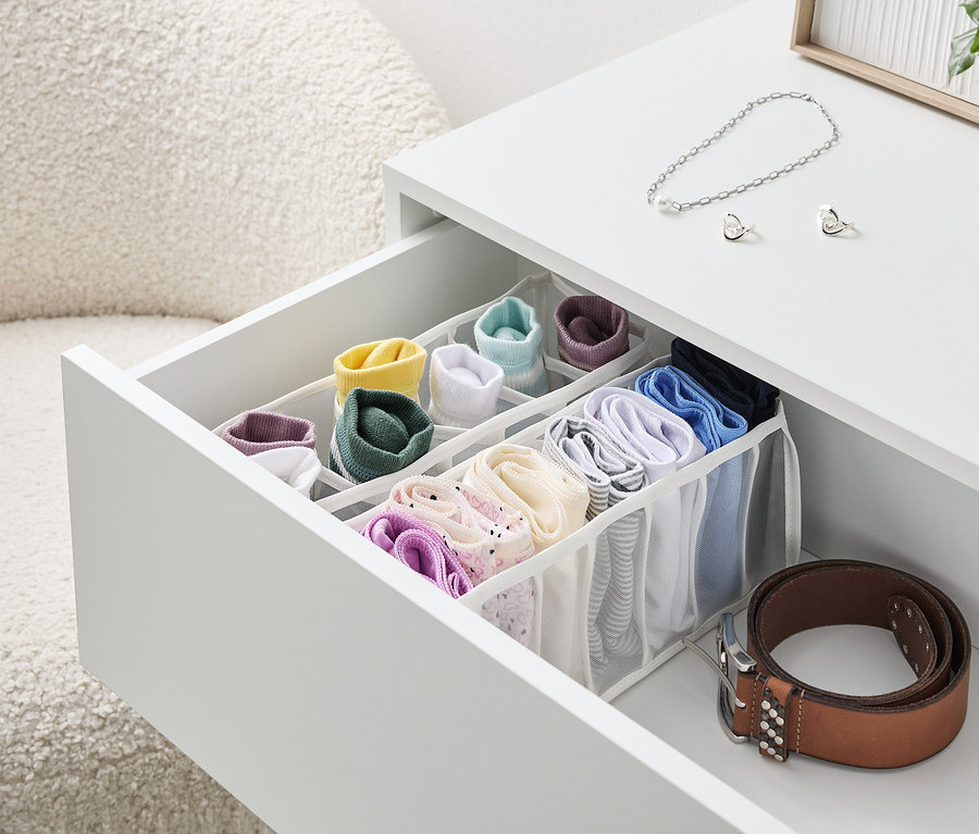 Ein offener Schubladentisch in Weiß mit einem Organizer voller bunter Socken und Unterwäsche, daneben liegt ein brauner Gürtel.