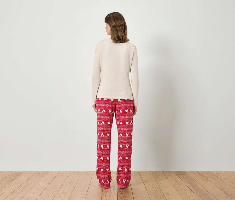Frau mit beigem Oberteil und roter Pyjamahose mit Mickey-Mouse-Motiv steht mit dem Rücken zur Kamera.