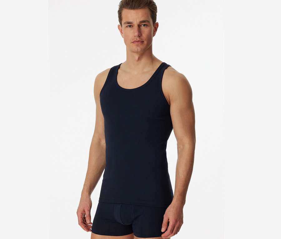 Mann posiert vor weißen Hintergrund in 2 blauen SCHIESSER Unterhemden in Feinripp.