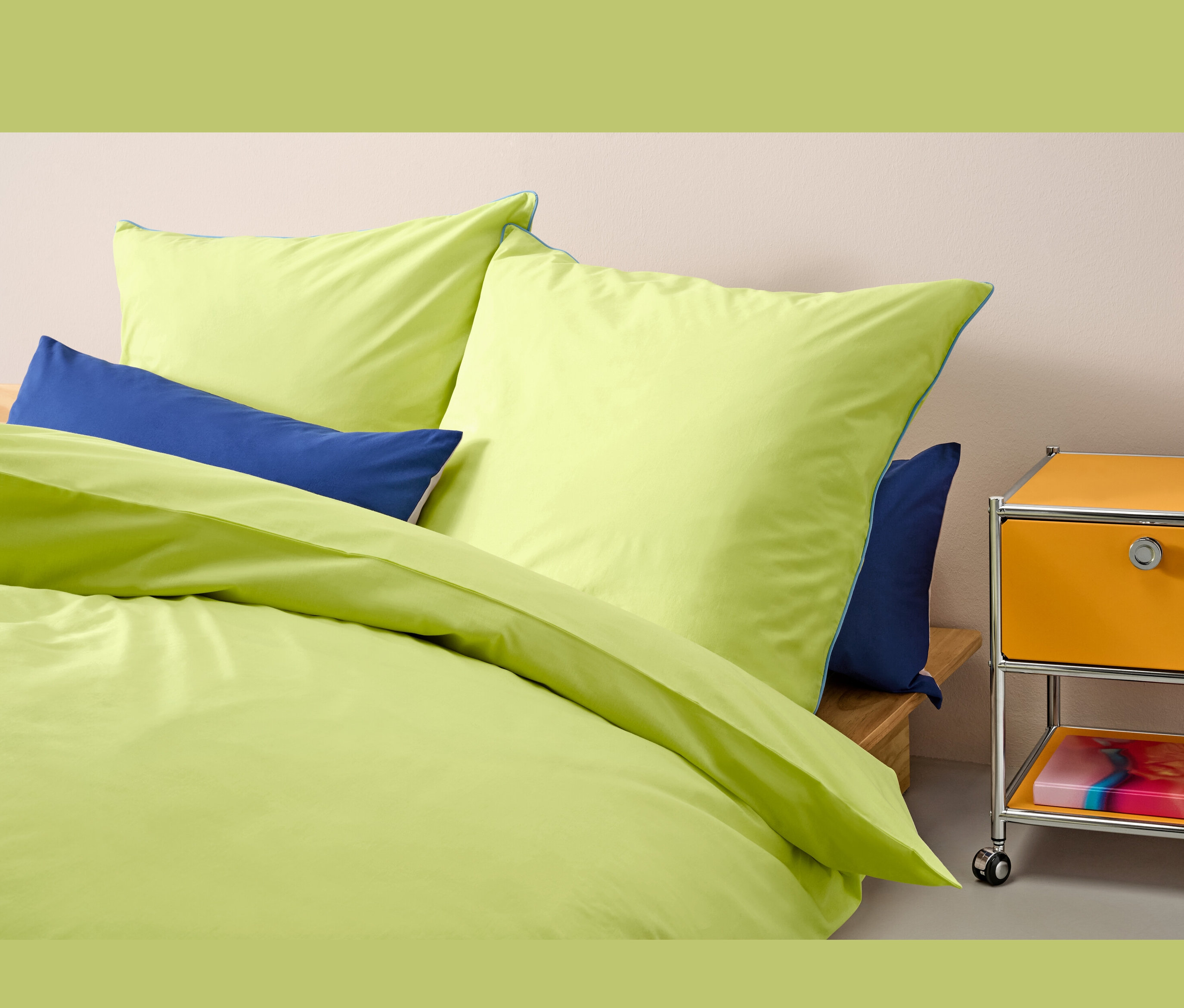 Gelbe Renforcé-Bettwäsche Normalgröße liegt auf einem Bett mit blauen Kissen.