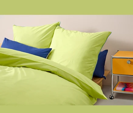 Gelbe Renforcé-Bettwäsche Normalgröße liegt auf einem Bett mit blauen Kissen.