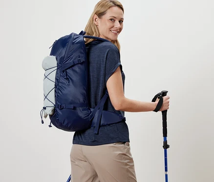 Frau mit Outdoor-Rucksack und Trekkingstöcken blickt über die Schulter.