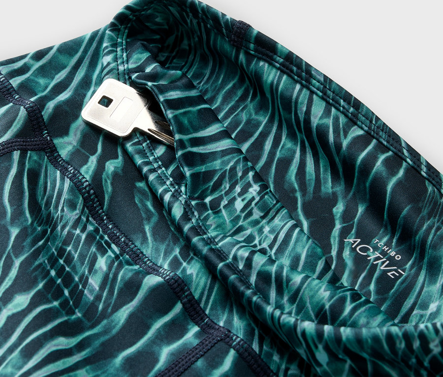 Detailaufnahme von grünen, gemusterten Sport-Tights mit einer Schlüsseltasche, in der ein Schlüssel steckt.