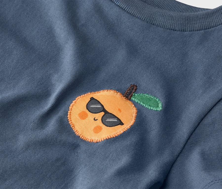 Nahaufnahme eines blauen T-Shirts mit einer aufgenähten Mandarine mit Sonnenbrille.