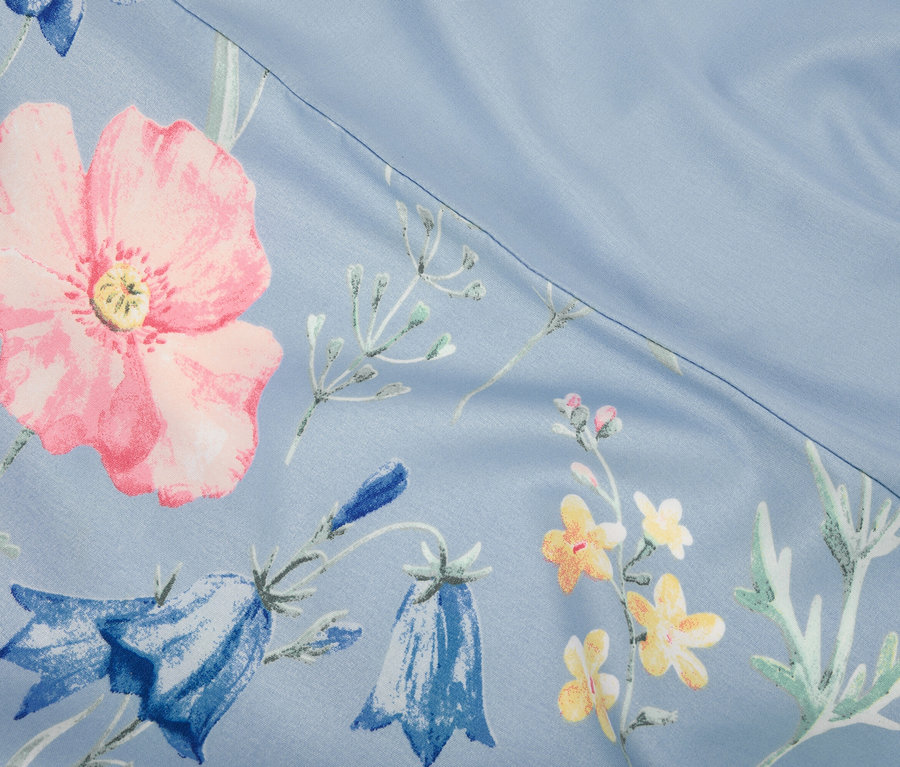 Nahaufnahme eines hellblauen Stoffes mit rosa Mohnblumen und blauen Glockenblumen.