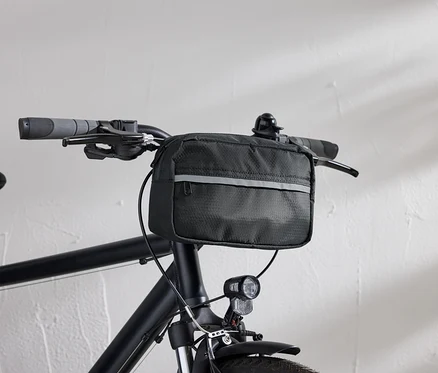 Detailansicht eines schwarzen Fahrrads mit einer schwarzen Lenkertasche und einem Fahrradlicht vor einer weißen Wand.
