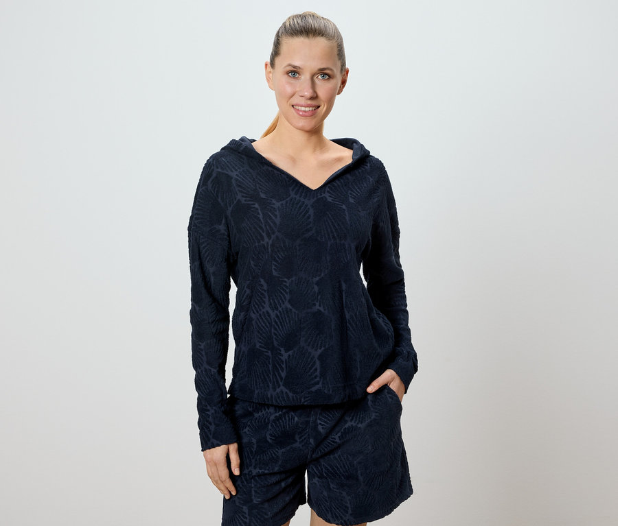 Frau trägt ein marineblaues Hoodie- und Shorts-Set mit einem Allover-Muschelmuster.