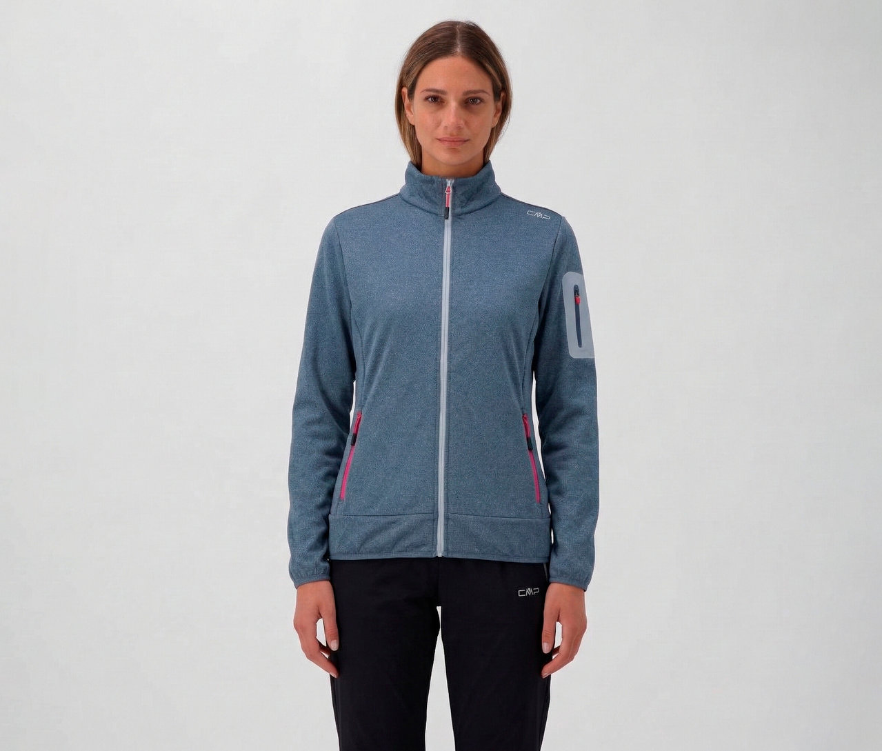 Frau mit blau melierter CMP Damen-Jacke mit durchgehendem Reißverschluss und schwarzen Hosen vor einem neutralen Hintergrund.
