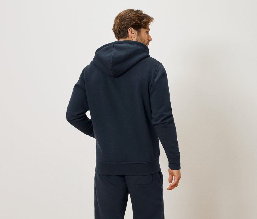 Rückansicht eines Mannes mit braunen Haaren, der einen marineblauen Hoodie und marineblaue Trainingshose trägt.