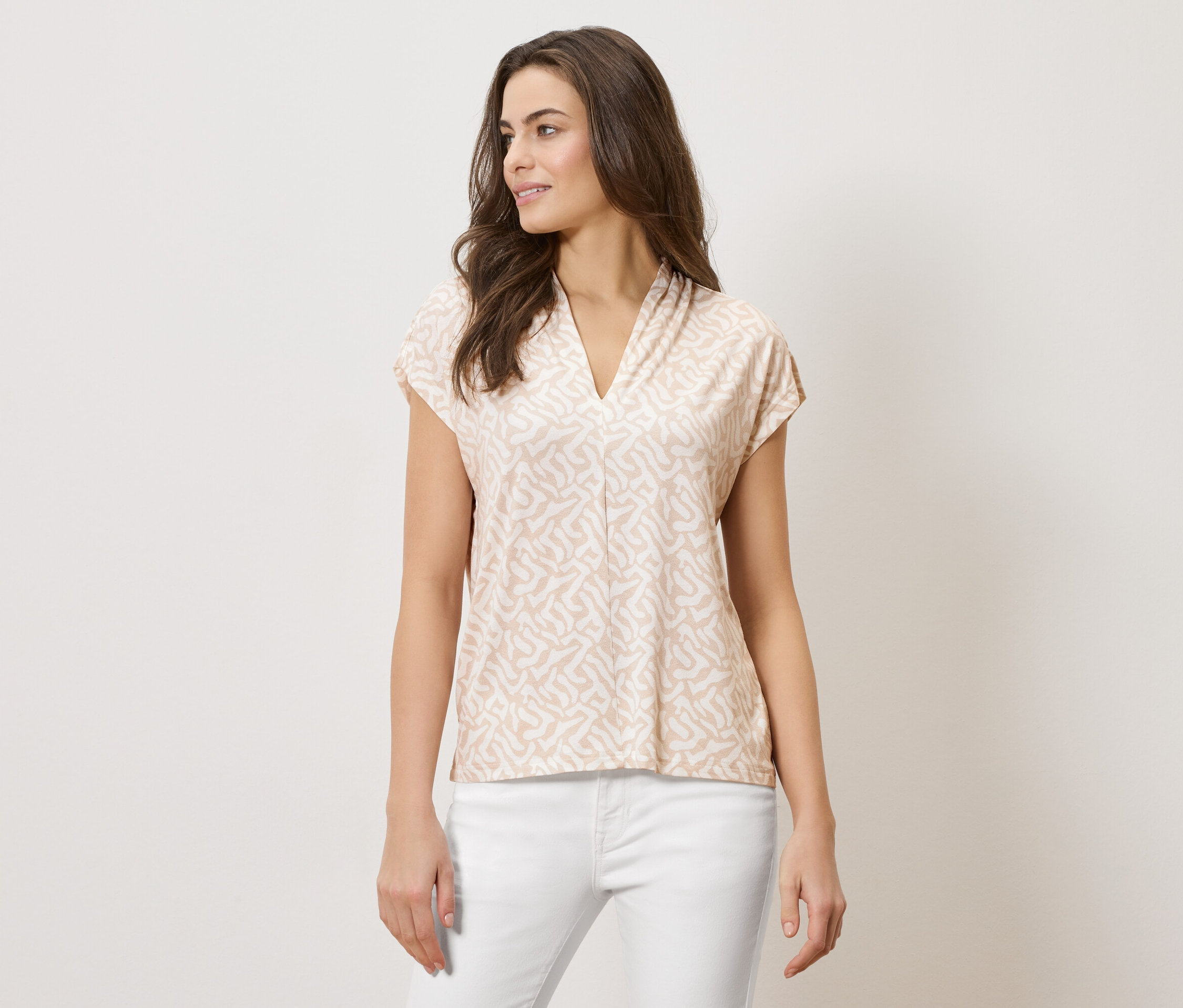 Frau trägt ein hellbraunes, gemustertes Oberteil mit V-Ausschnitt und weiße Hosen.