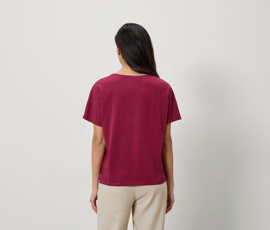 Rückansicht einer Frau mit langen dunklen Haaren, die ein weinrotes T-Shirt und eine beige Hose trägt.