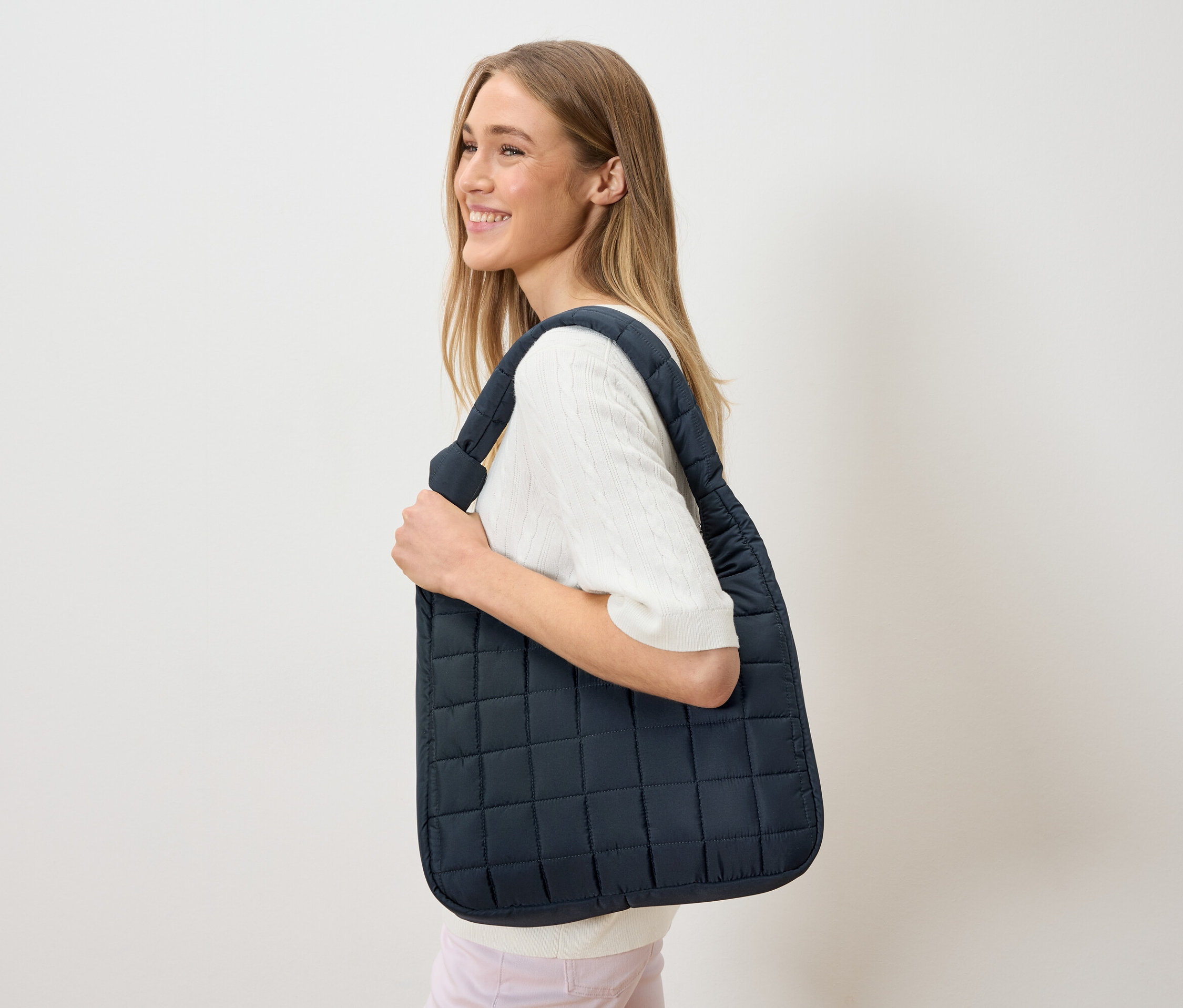 Frau trägt eine marineblaue, gesteppte Tragetasche über der Schulter.