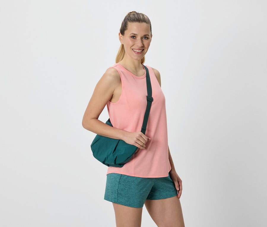Frau mit einem grünen Seesack über ihrer Schulter, gekleidet in ein rosa Tanktop und grüne Shorts.