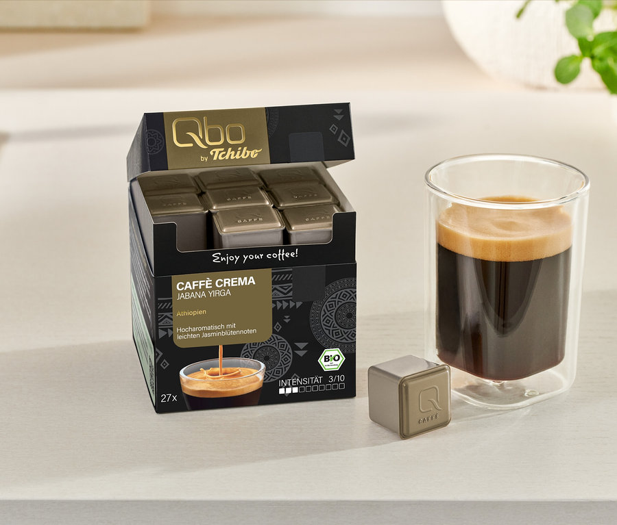 Geöffneter Karton Qbo Caffè JABANA YIRGA mit Kapseln, Tasse Kaffee und einzelne Kapsel auf einer hellen Oberfläche.