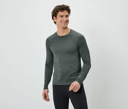 Mann mit lockigem Haar, trägt ein graues Langarmshirt und schwarze Leggings, lächelt und blickt nach rechts vor einem weißen Hintergrund.