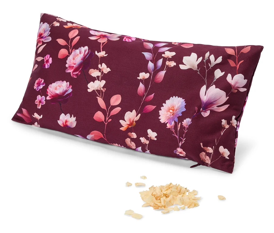 Ein rechteckiges Kissen mit dunkelrotem Hintergrund und einem Blumenmuster aus rosa, lila und weißen Blüten und Blättern. Daneben liegt ein kleiner Haufen heller, flockiger Füllung.