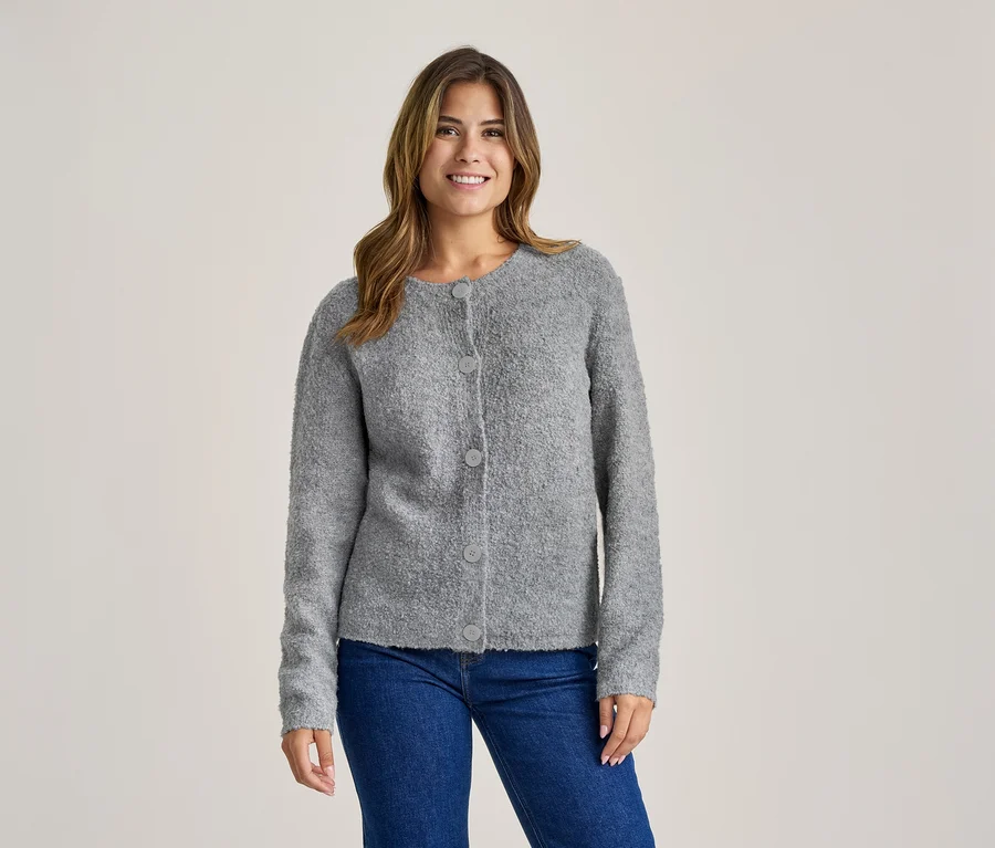 Lächelnde Frau in einer grauen, strukturierten Strickjacke mit Knöpfen und blauen Jeans.