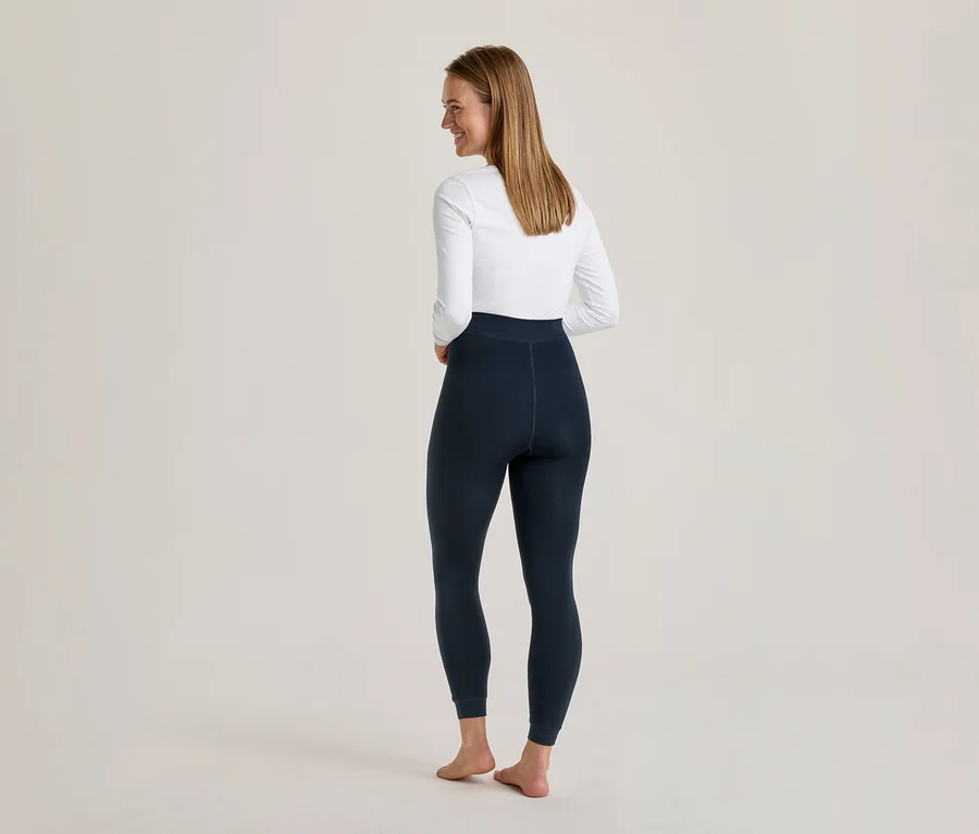 Frau von hinten, lächelnd über die Schulter blickend, trägt weißes Langarmshirt und dunkelblaue Leggings.
