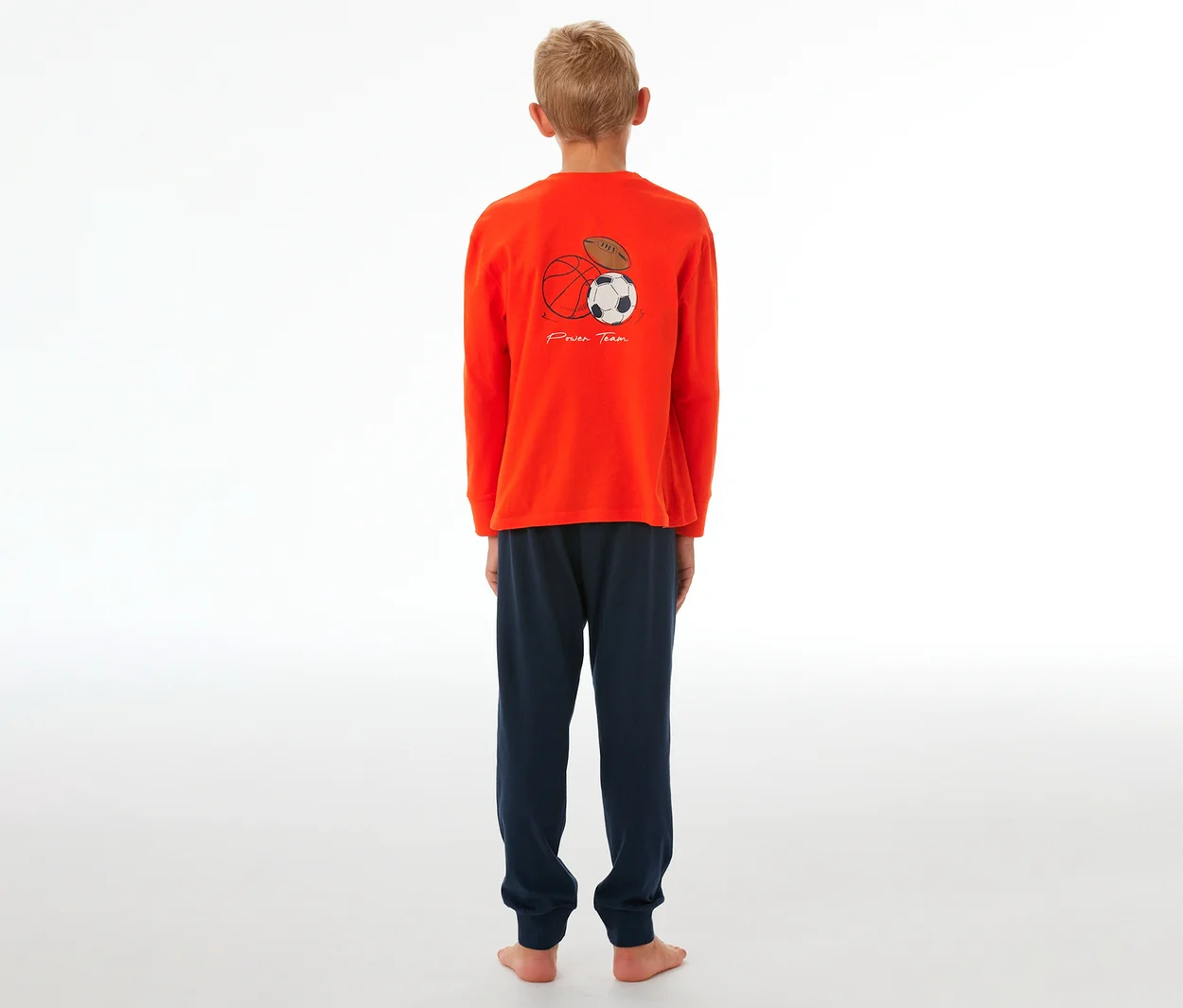 Junge in SCHIESSER Kinder-Pyjama mit Bündchen, orangefarbenes Oberteil mit Sportball-Grafik und marineblauer Hose.