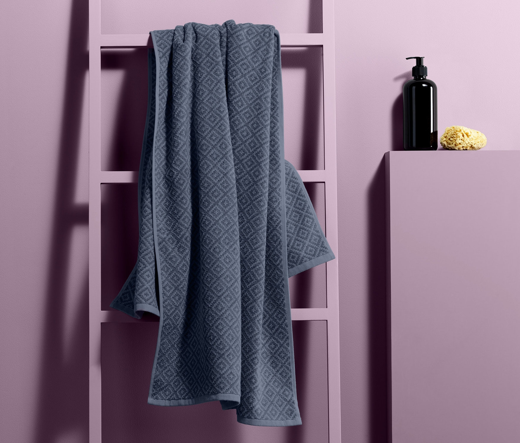 Ein Jacquard-Badetuch hängt auf einer Dekoleiter neben einem Seifenspender und einem Schwamm.