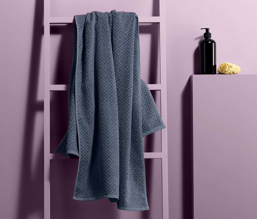 Ein Jacquard-Badetuch hängt auf einer Dekoleiter neben einem Seifenspender und einem Schwamm.