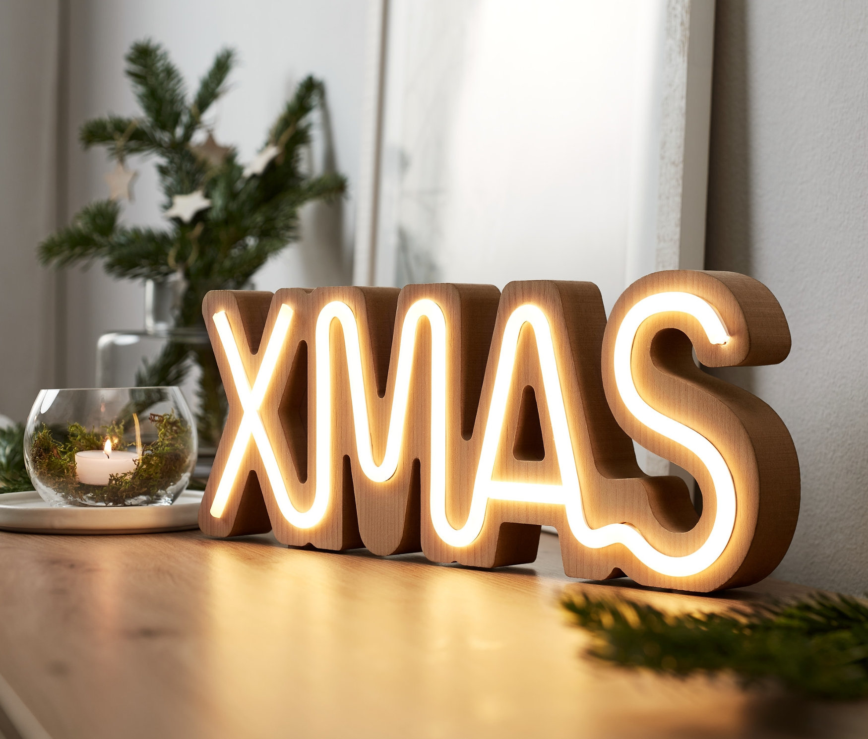 LED-Schriftzug "XMAS" steht auf einer Kommode.