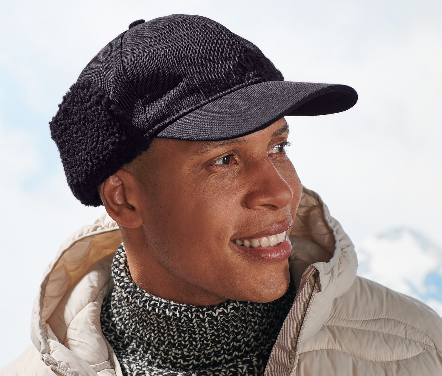 Mann lächelt und trägt eine beige Jacke und eine Funktionscap.