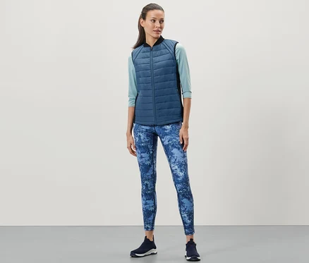 Frau trägt eine Thermo-Steppweste, blaue Leggings und dunkle Turnschuhe.