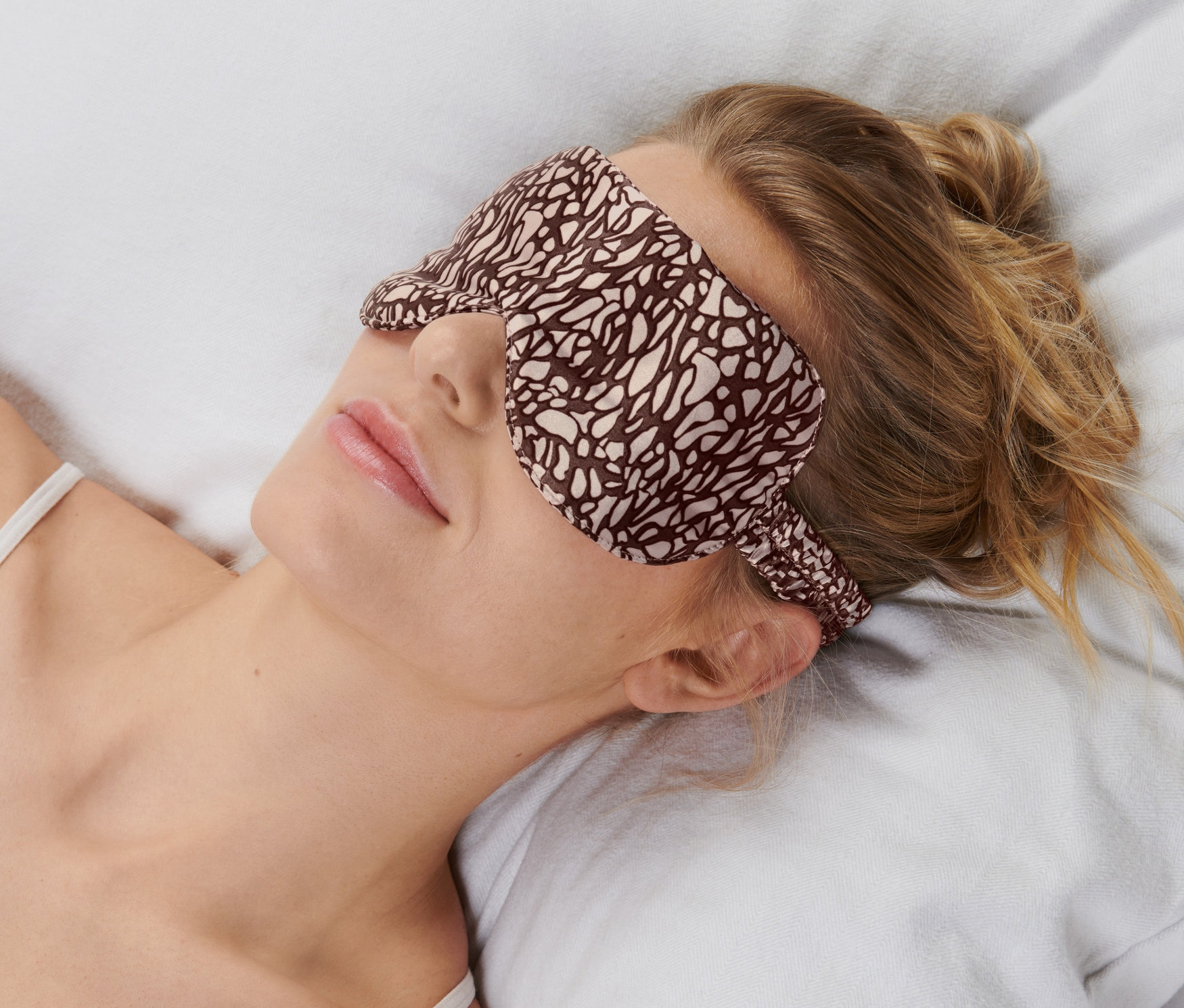 Frau liegt mit einer Schlafmaske auf einem Kissen.