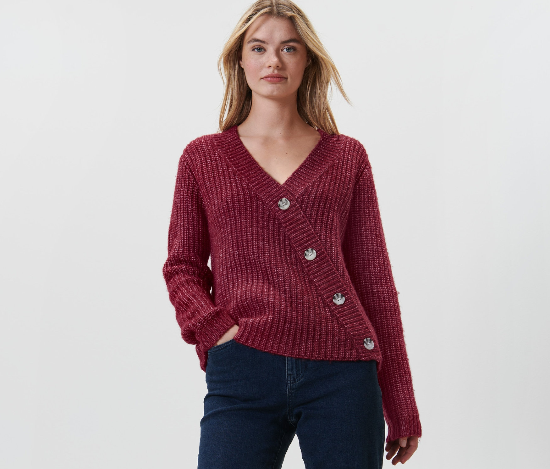 Frau posiert in rotem Grobstrick-Cardigan und dunkler Jeans.