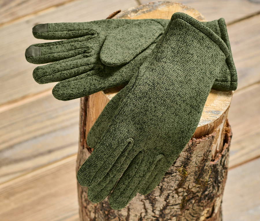 Khakifarbene Strickfleece-Handschuhe liegen auf einem Holzscheit.