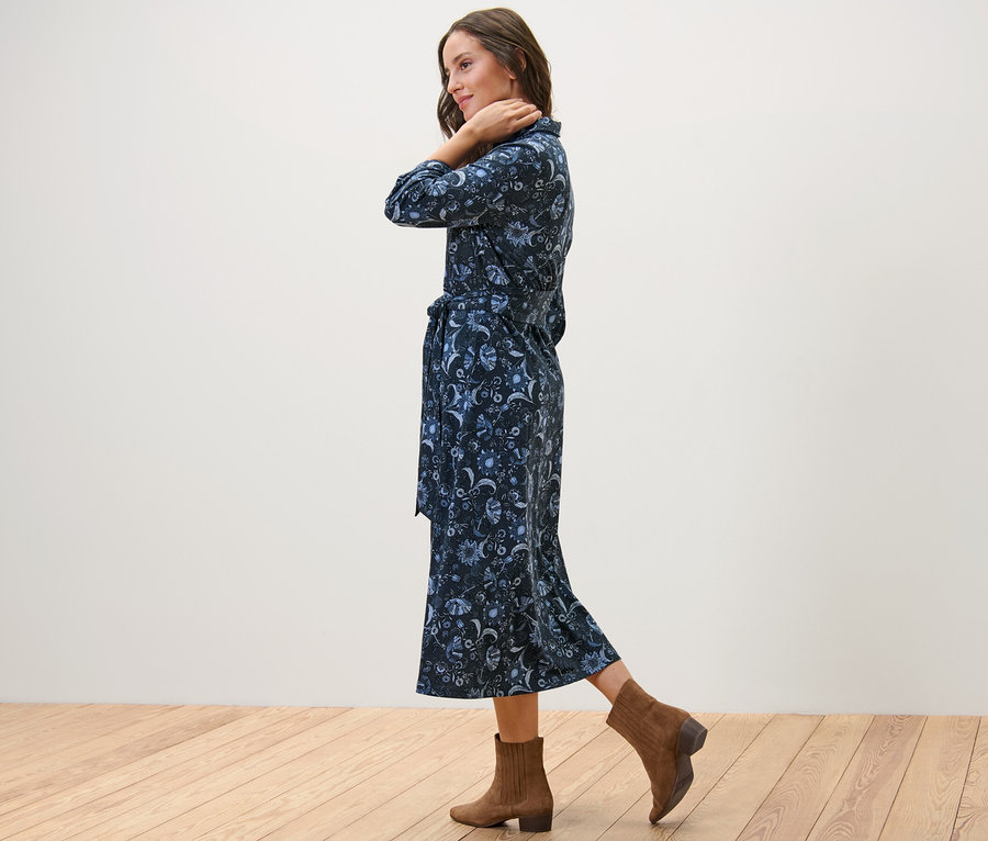 Frau posiert seitlich in einem bedruckten Jerseykleid und braunen Stiefeletten.