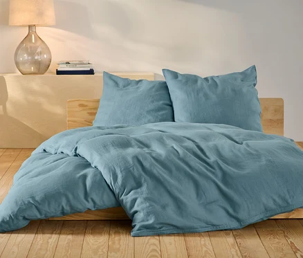 Blaue Leinen-Bettwäsche in Normalgröße und Übergröße auf einem Bett.