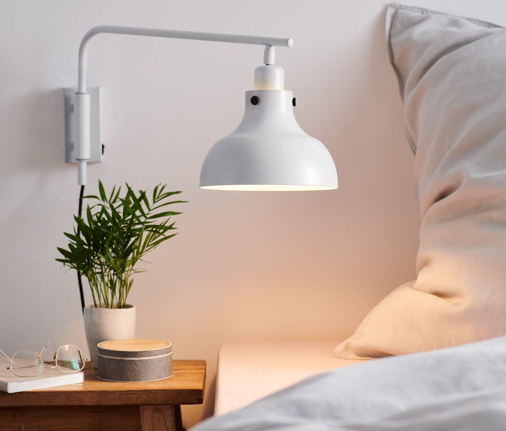 Wandleuchte mit Schwenkarm aus Metall beleuchtet Nachttisch mit Pflanze.