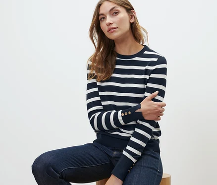 Frau sitzt auf einem Hocker und trägt einen gestreiften Feinstrickpullover in Navy.